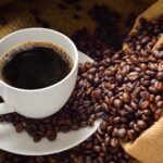 Roasted coffee beans and a brewed cup of coffee in a white mug