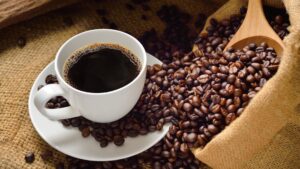 Roasted coffee beans and a brewed cup of coffee in a white mug