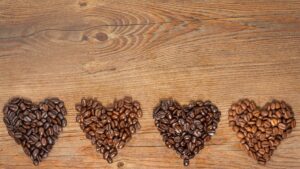 Different toasts of coffee beans gathered into four heart shapes on a board.