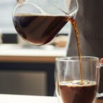 Barista pouring freshly brewed coffee into a glass mug.